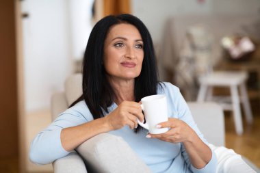 Gülümseyen olgun bir kadının portresi sıcak kahve içiyor.