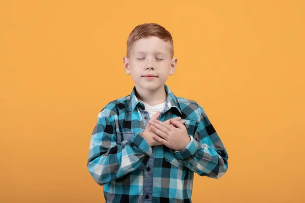 Adorable redhead boy with eyes closed holding hands on heart — Stock Photo, Image