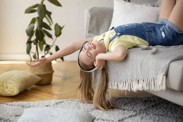 Dospívající dívka ležící vzhůru nohama na gauči, poslouchající hudbu — Stock fotografie