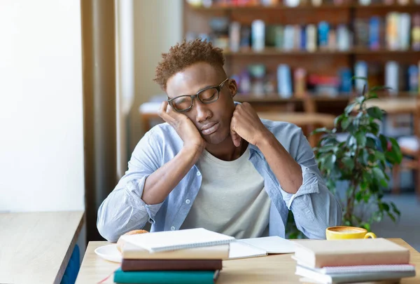 Tipo negro cansado con un montón de libros estudiando para el examen en la cafetería urbana — Foto de Stock