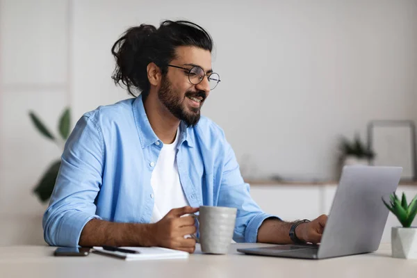 Pros de Freelancing. Positivo Freelancer Guy Beber café y trabajar en el ordenador portátil —  Fotos de Stock