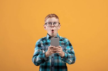 Surprised schoolboy playing game on smartphone, yellow background