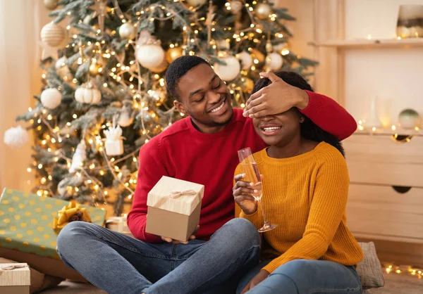 Παρουσιάζει χρόνο στο σαλόνι. Χαμογελώντας ο νεαρός Αφροαμερικάνος σύζυγος κλείνει τα μάτια στη γυναίκα — Φωτογραφία Αρχείου