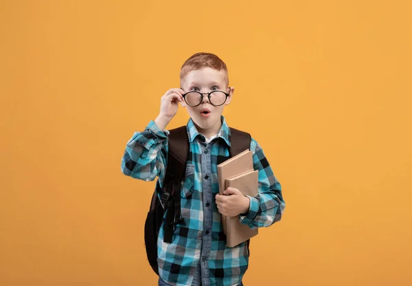 Zaskoczony uczeń w okularach trzymający książki na żółtym tle — Zdjęcie stockowe
