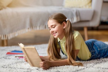 Kid lying on floor carpet, holding and reading book