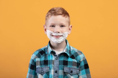 Oyuncu küçük çocuk sarı arka planda yüzünü tıraş ediyor.