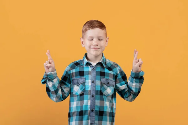 Позитивный ребенок с закрытыми глазами, показывающий скрещенные пальцы — стоковое фото