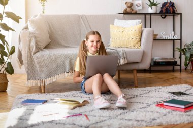 Öğrenci yerde oturuyor ve bilgisayarını kullanıyor.