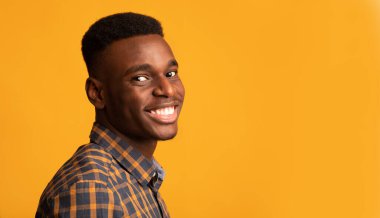 Young African American Guy Smiling To Camera, Standing Half-Turned Over Yellow Background