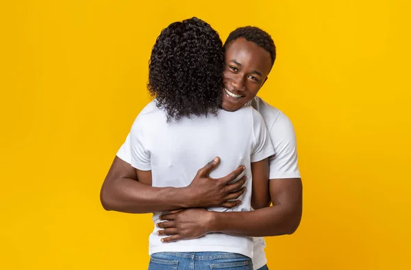 Happy black guy hugging his girlfriend, yellow background — Stockfoto