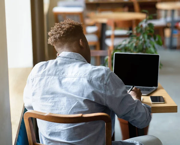 Back view of young black male student studying online on laptop at city cafe, mockup for website design on screen — Stock Fotó