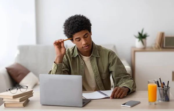 Réfléchi noir adolescent guy passer examen dur ou test en ligne sur ordinateur portable à la maison — Photo