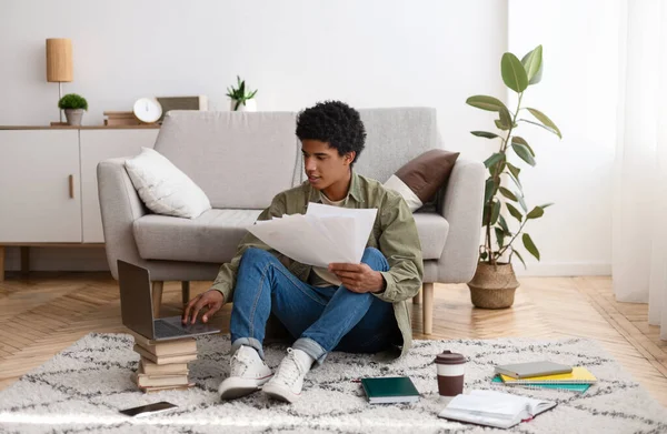 Young teen guy with educational materials, books and laptop computer working on cousework or school project at home — Foto de Stock