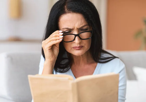 Maturo confuso donna in occhiali cercando di leggere libro — Foto Stock