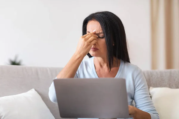 Fatigued upset mature woman massaging nose bridge, using laptop — Stockfoto