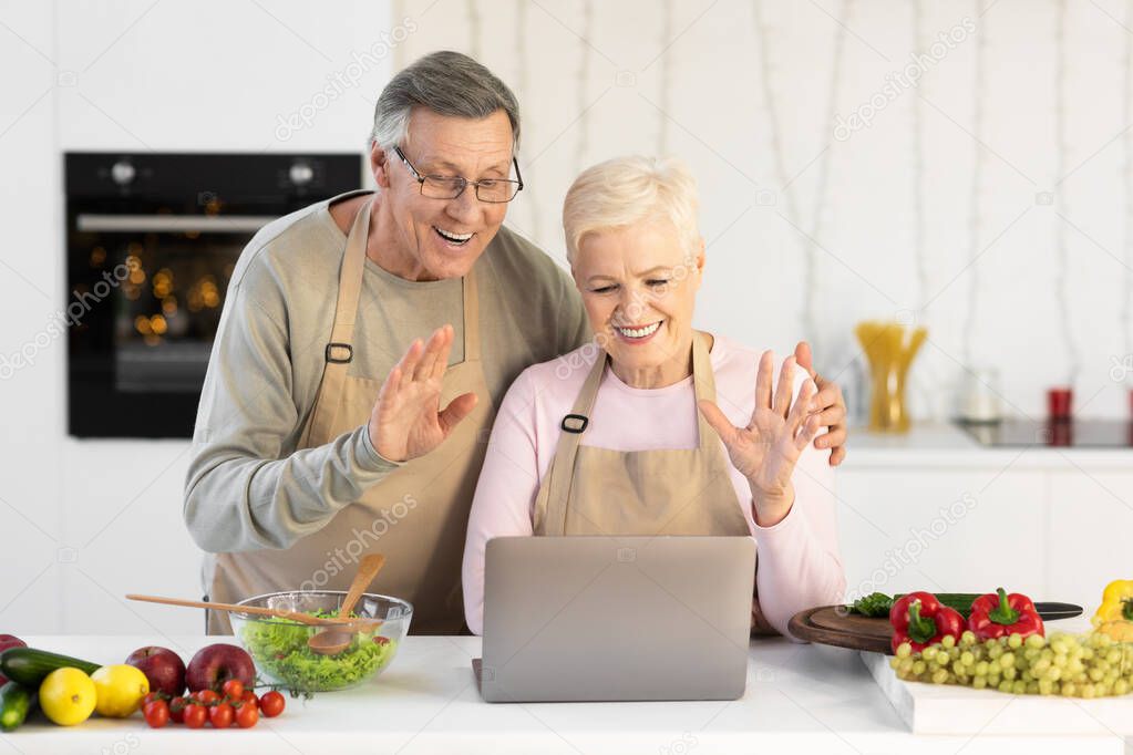 Joyful Senior Couple Video Calling Online Using Laptop In Kitchen