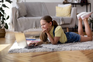 Kız yerde yatıyor ve dizüstü bilgisayarını kullanıyor.