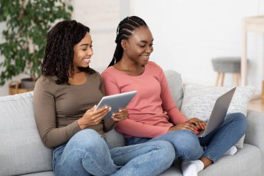 Two african girlfriends spending time at home, using gadgets