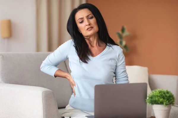 Mature woman having back pain while using laptop — Stock Photo, Image