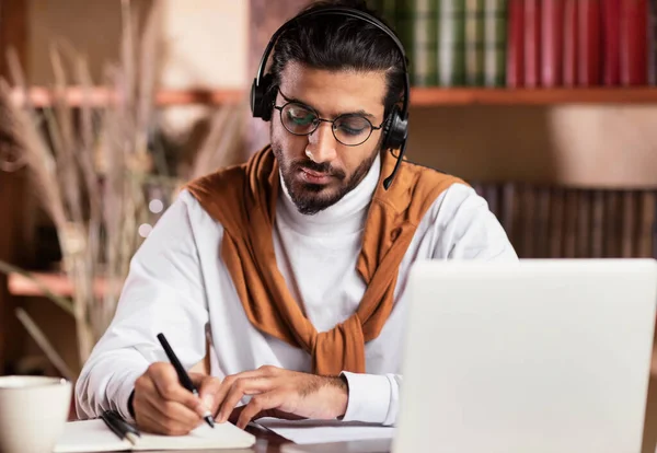 Indian Guy Taking Notes Learning At Laptop Online At Home