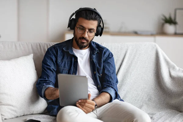 Chico indio pasar tiempo en casa con tableta digital y auriculares inalámbricos —  Fotos de Stock