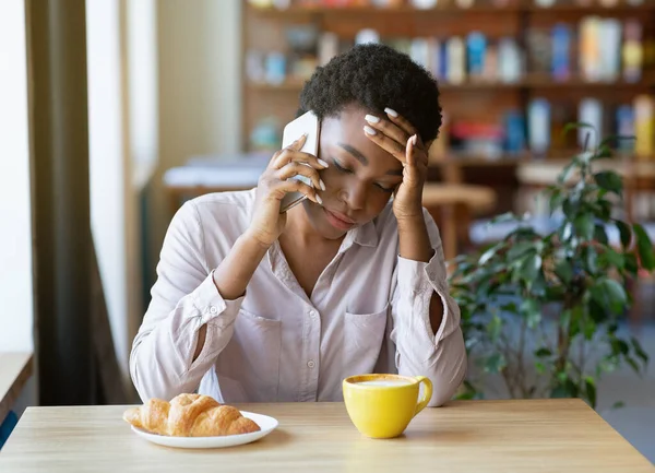 Расстроенная черная леди, разговаривающая на смартфоне во время завтрака в городском кафе — стоковое фото