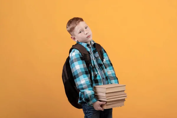 Kimerült iskolás fiú hátizsákkal egy halom könyvet tart. — Stock Fotó