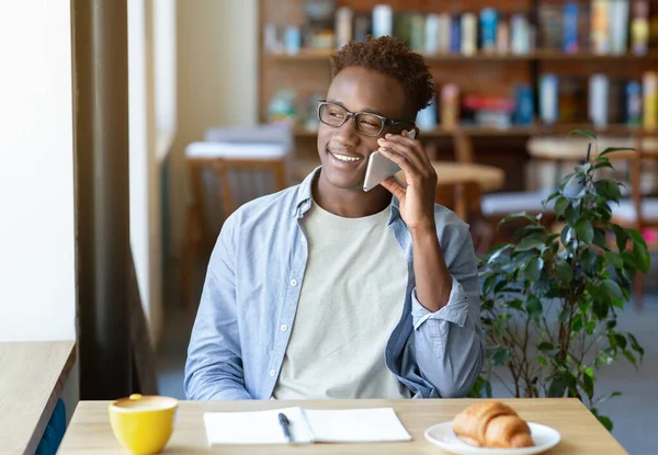 Glad svart student talar på mobiltelefon under sina studier på urban café — Stockfoto