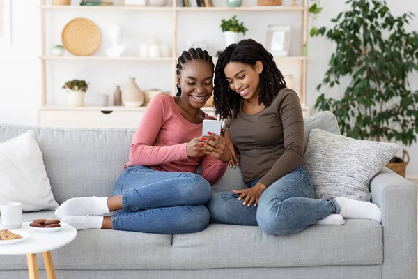 Glada svart flickvän sitter på soffan och använder smartphone — Stockfoto