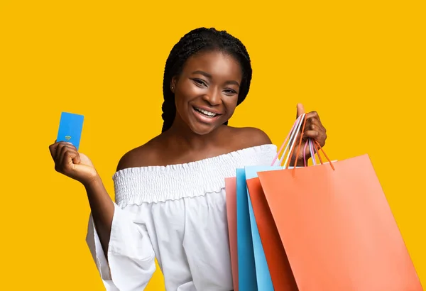 Pagos fáciles. Sonriente joven negro sosteniendo tarjeta de crédito y bolsas de compras —  Fotos de Stock