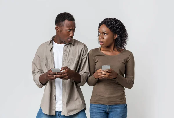 Annoyed black couple with smartphones looking at each other — Stock Photo, Image