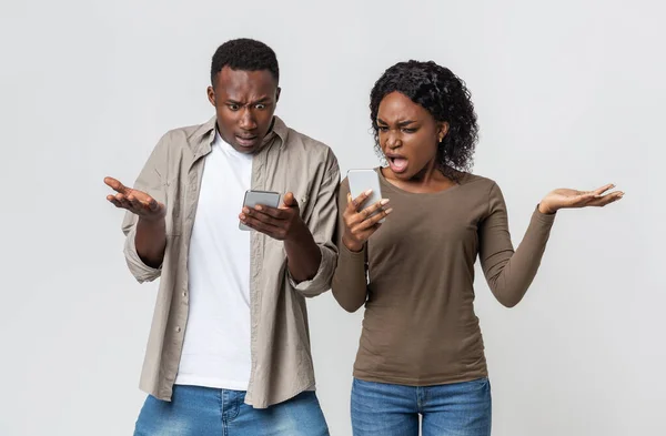 Furious black couple holding mobile phones, gesturing — Stock Photo, Image