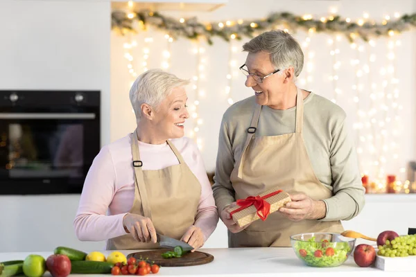 Esposo mayor dando a esposa regalo de Navidad celebrando vacaciones en la cocina —  Fotos de Stock