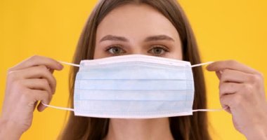Koruyucu tıbbi maske takan genç bir kadının portresi, turuncu stüdyo arka planı, yavaş çekim.