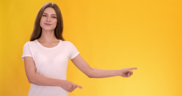 Young woman pointing finger at copy space, showing mockup for advertisement, orange studio background — ストック動画