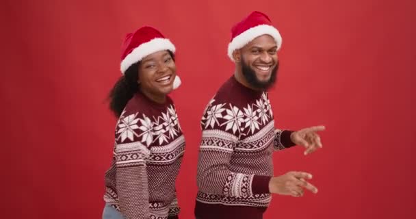 Feliz homem americano africano alegre e mulher em chapéus santa dançando sobre fundo estúdio vermelho, diversão festa de Natal — Vídeo de Stock