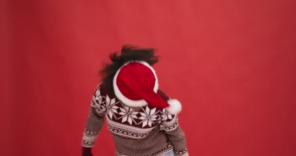 Giovane donna afroamericana in maglia maglione e cappello di Babbo Natale danza, illuminazione alla festa di Natale, sfondo rosso — Video Stock