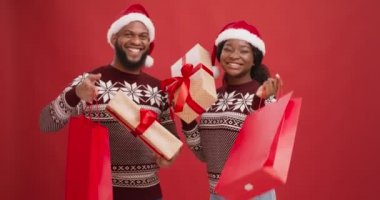 Noel alışverişi. Noel Baba şapkalı neşeli Afro-Amerikan çift ellerinde hediye kutuları ve alışveriş torbaları var.