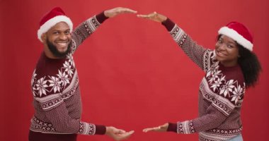 Güzel bir Noel teklifi. Noel Baba şapkalı mutlu Afro-Amerikan çifti elleri, kırmızı arka planı, boş alanı olan bir çerçeve yapıyorlar
