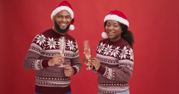 Festa di Capodanno. Giovane felice coppia nera in cappelli di Natale ballare con champagne su sfondo rosso studio — Video Stock