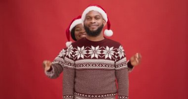 Noel Baba şapkalı mutlu Afro-Amerikan kadın sevgilisinin gözlerini kapatıyor, birlikte eğleniyor, kırmızı stüdyo geçmişi var.