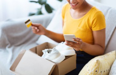 Kutu, kredi kartı ve akıllı telefonla oturan mutlu siyah kadın.