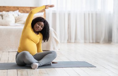 Neşeli zenci hamile kadın evde sabah egzersizi yapıyor.