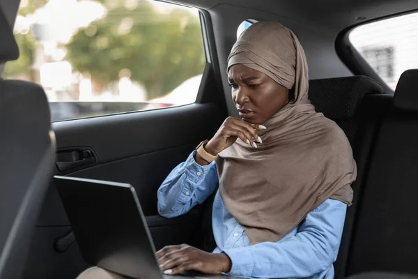 Empresaria islámica negra estresada que trabaja en el ordenador portátil en el asiento trasero del coche — Foto de Stock