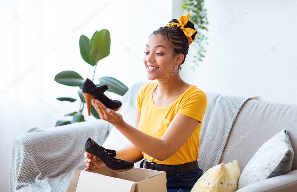 Happy black woman unpacking parcel with clothing and shoes