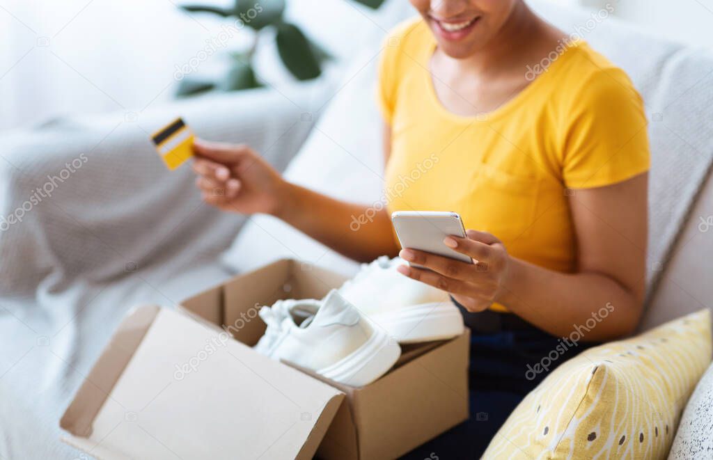 Happy black woman sitting with box, credit card and smartphone