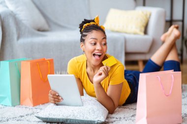 Evde tablet ve kredi kartı kullanan siyah bir kadın.