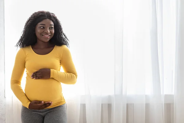 Wanita afrika hamil yang cantik memeluk perutnya yang besar di rumah — Stok Foto