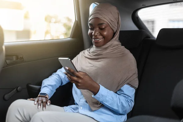 Zwarte moslim zakenvrouw in hijab met behulp van smartphone tijdens het reizen met de auto — Stockfoto