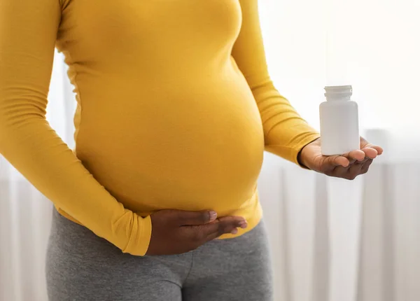 Невпізнавана чорна вагітна жінка тримає білу банку з таблетками — стокове фото